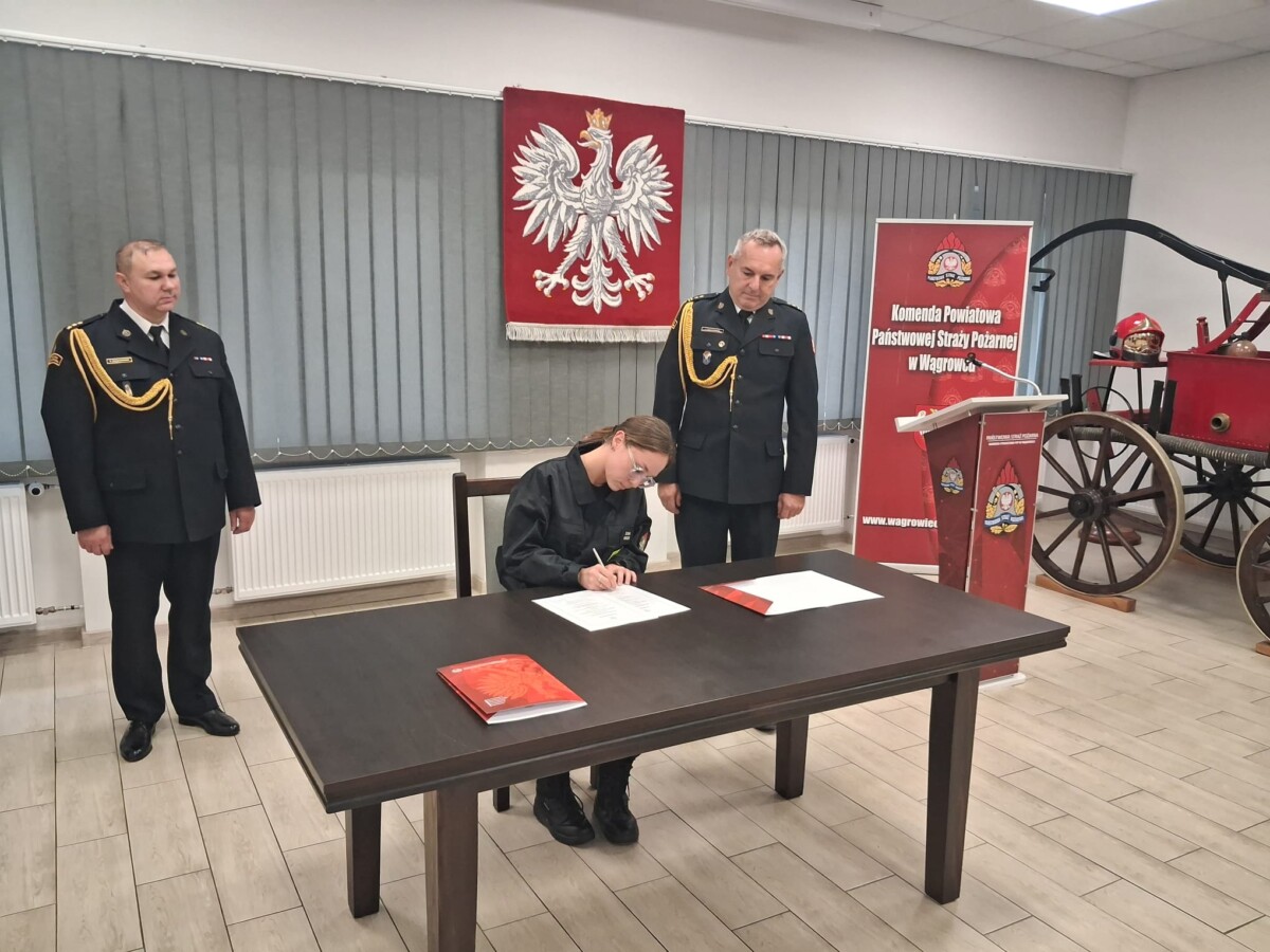 Na zdjęciu widać funkcjonariuszkę podczas podpisywania dokumentów w obecności kierownictwa Komendy Powiatowej PSP